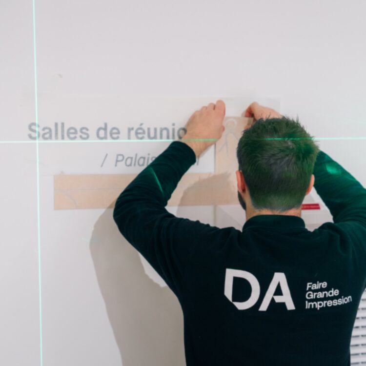 Applicateur DecoAder posant un lettrage adhésif mural avec un mètre laser pour une signalétique précise.